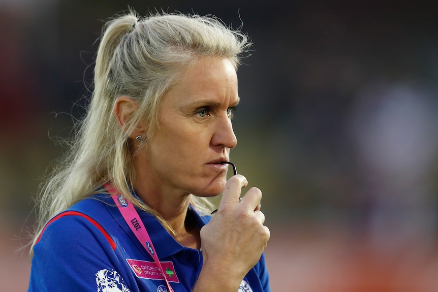 A Western Bulldogs AFLW coach stares to her left as she holds her glasses.