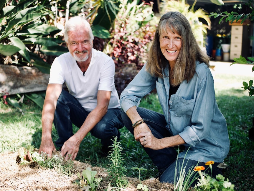 A woman and a man smile as they inspect a garden bed