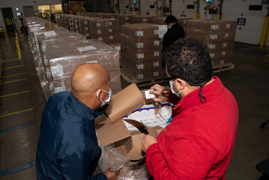 Two men inspecting a box full of pills 