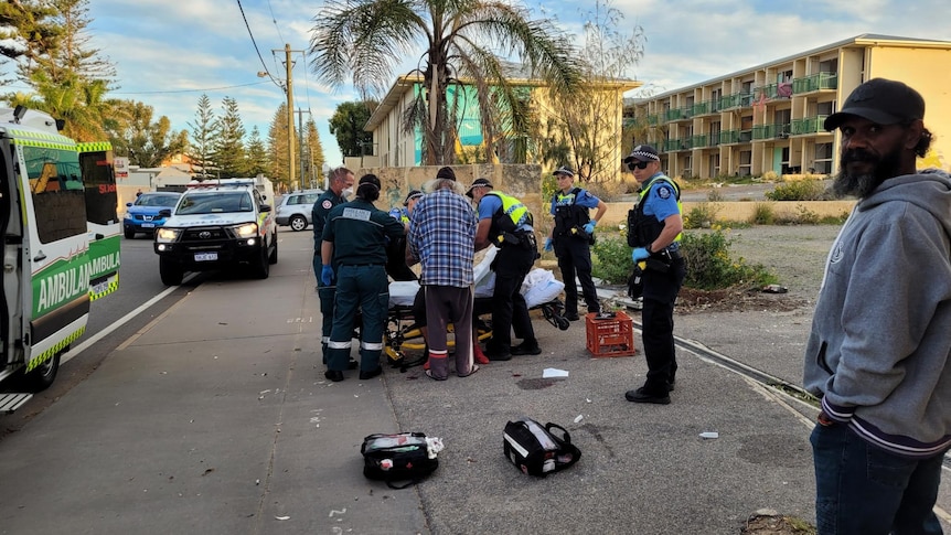 Man lies on stretcher surrounded by ambulance officers and police