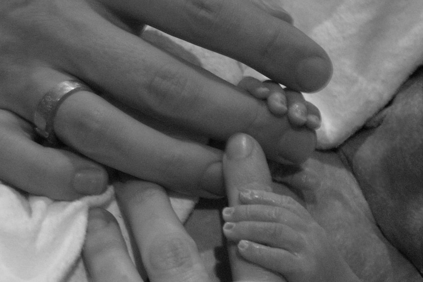 Little baby hands are wrapped around a mother's fingers.