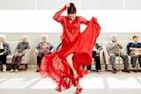 Pepa Molina dressed in red, dancing in a nursing home, surrounded by elderly people.