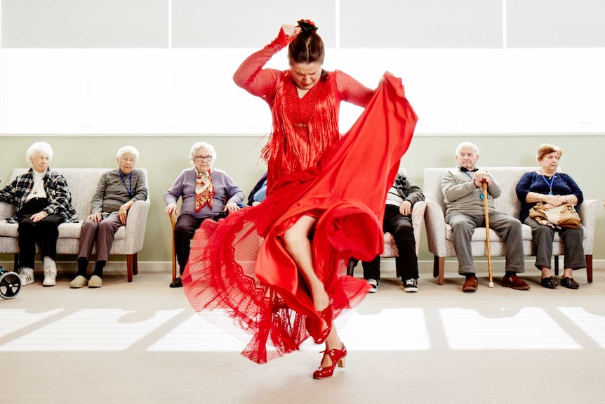 Pepa Molina dressed in red, dancing in a nursing home, surrounded by elderly people.