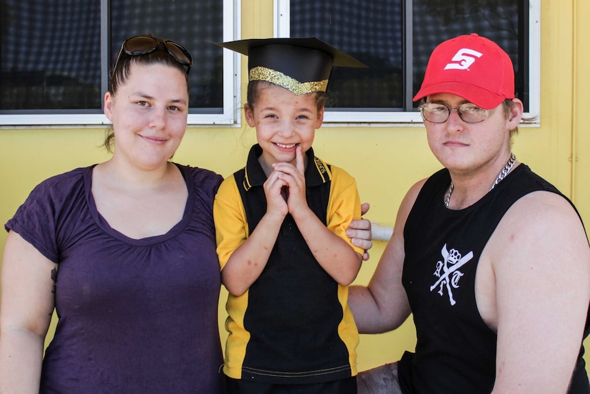 A prep-graduate wearing a glittery mortarboard stands with her parents.