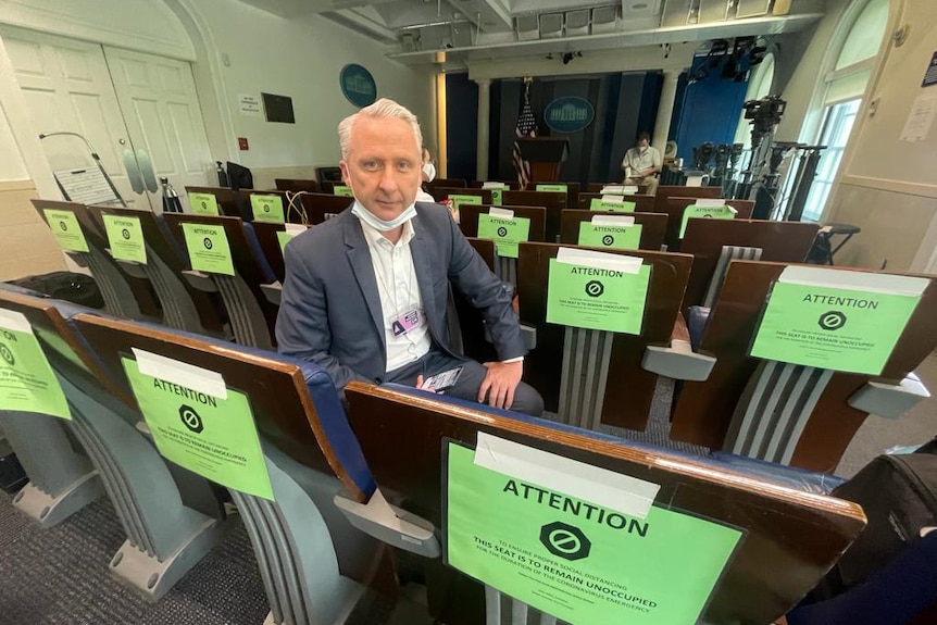 Man sitting in a row of chairs in briefing room with green warning signs on them.