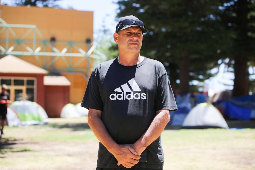 Mr Windus looks into the distance. He stands in front of  a collection of tents.