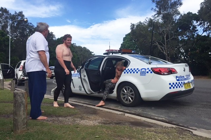 One of the rescued divers, Dylan Briggs (centre), stands next to a police car.