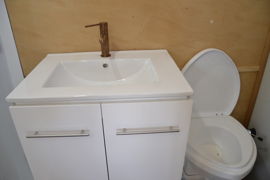A white sink and cabinet and toilet in a tiny home bathroom.