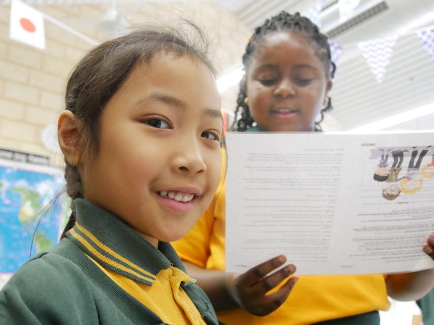 Two young girls in a primary school classroom looking at paper.