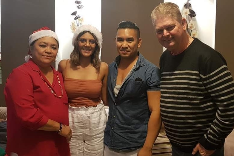 Four people stand arm-in-arm, some wearing Christmas gear.