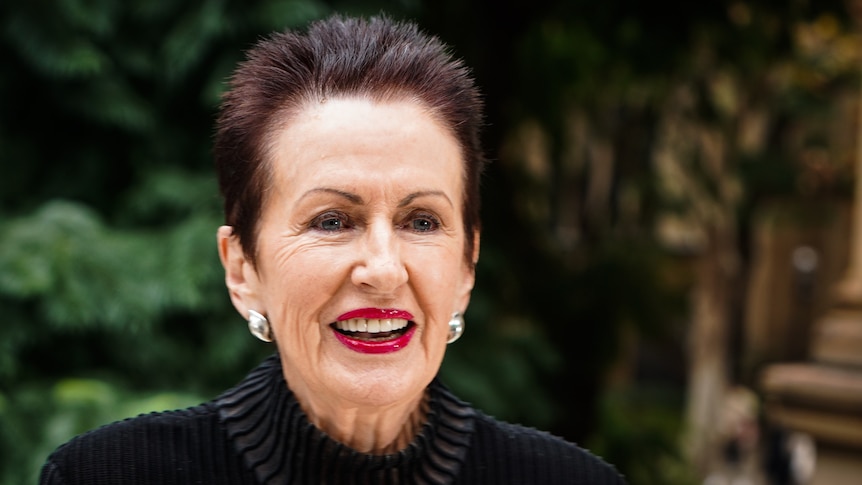 A smiling, older woman with short, dark hair, large earrings and a dark top.