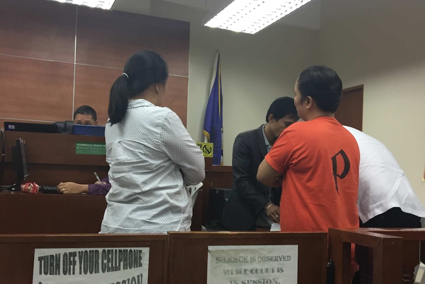 A woman in an orange top standing before a judge in a court room