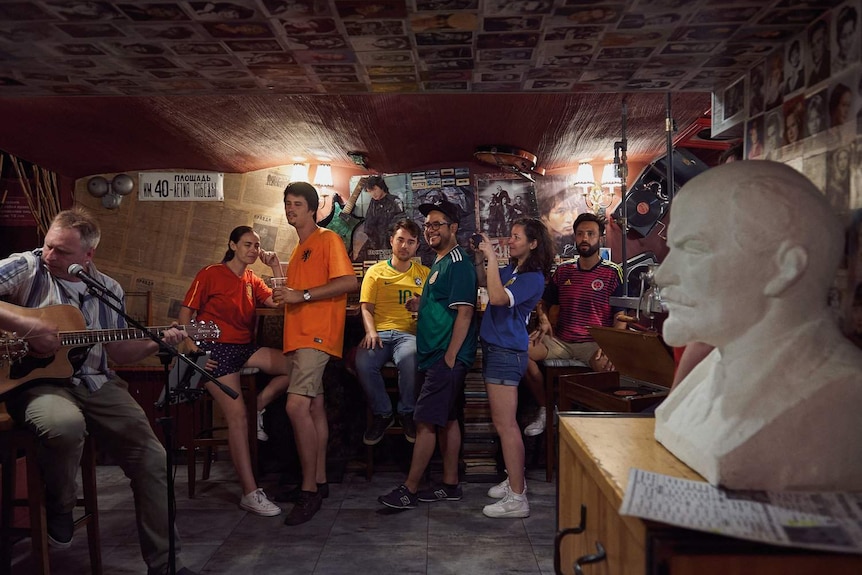 People wearing different coloured jerseys sit in a row in a music venue.