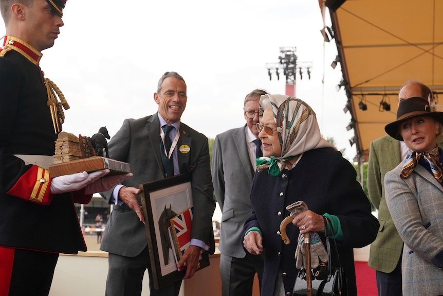 The Queen looks at a horse statue held by an officer in front of other smiling people