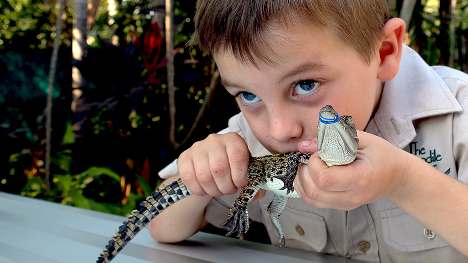 A boy kisses a baby crocodile.