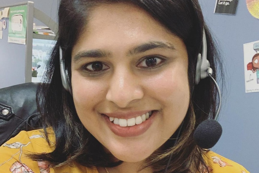 A smiling young woman wearing headphones with a microphone attached. 