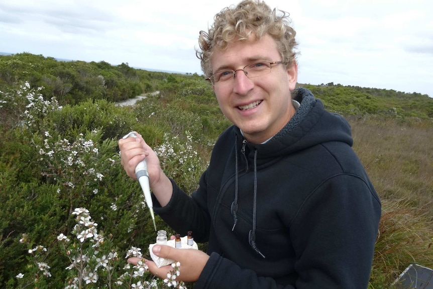 Simon smiling at the camera in front of leptospermum bushes in a national park.