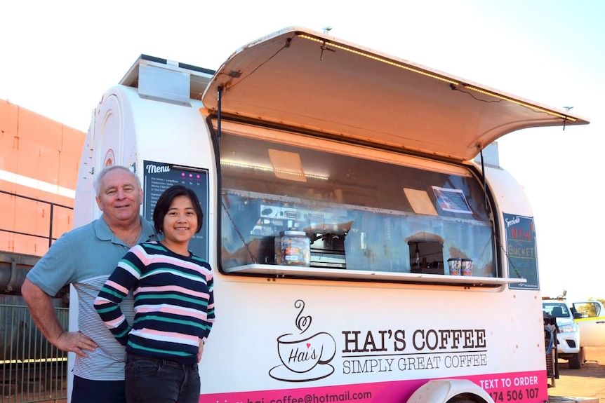 A man and woman stand alongside a trailer converted into a mobile coffee shop.