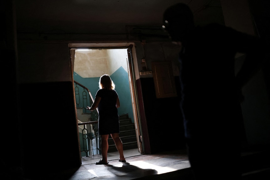 A woman stands in a dimly lit doorway. 