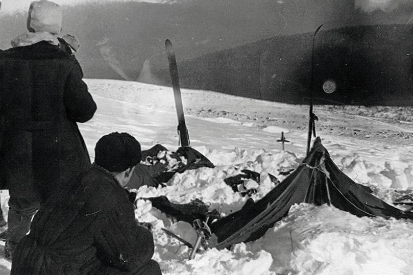 A black and white photo of a flattened, torn tent in the snow.