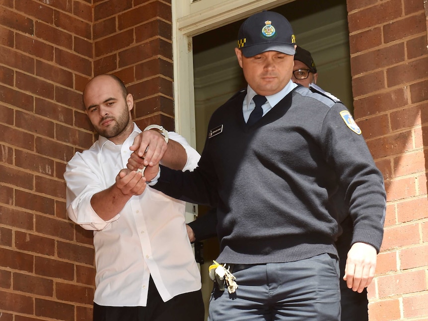 Vincent Stanford is escorted by correctional service officers from Griffith Local Court in a white shirt and handcuffs.