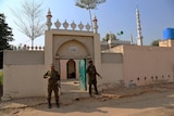 Two police armed with rifles guard the small gated entrance to a rural mosque.