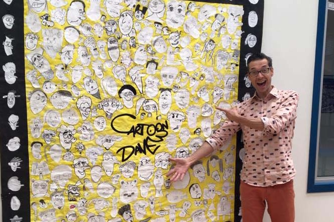Author and cartoonist Dave Hackett stands next to a board of cartoon heads