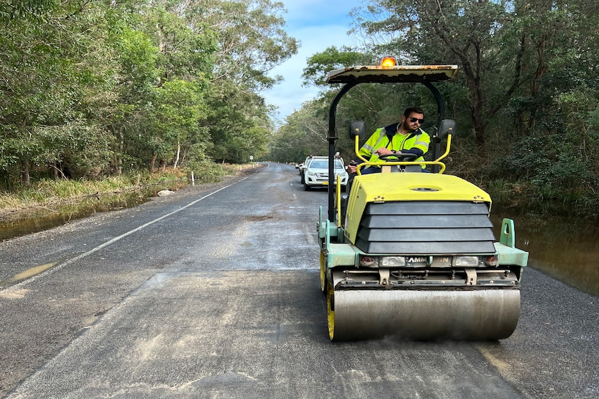 A council worker drives a roller over a freshly fixed section of road.