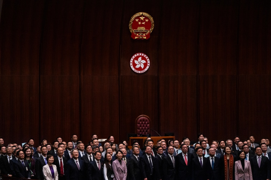A group of people stand below the red Hong Kong flag.