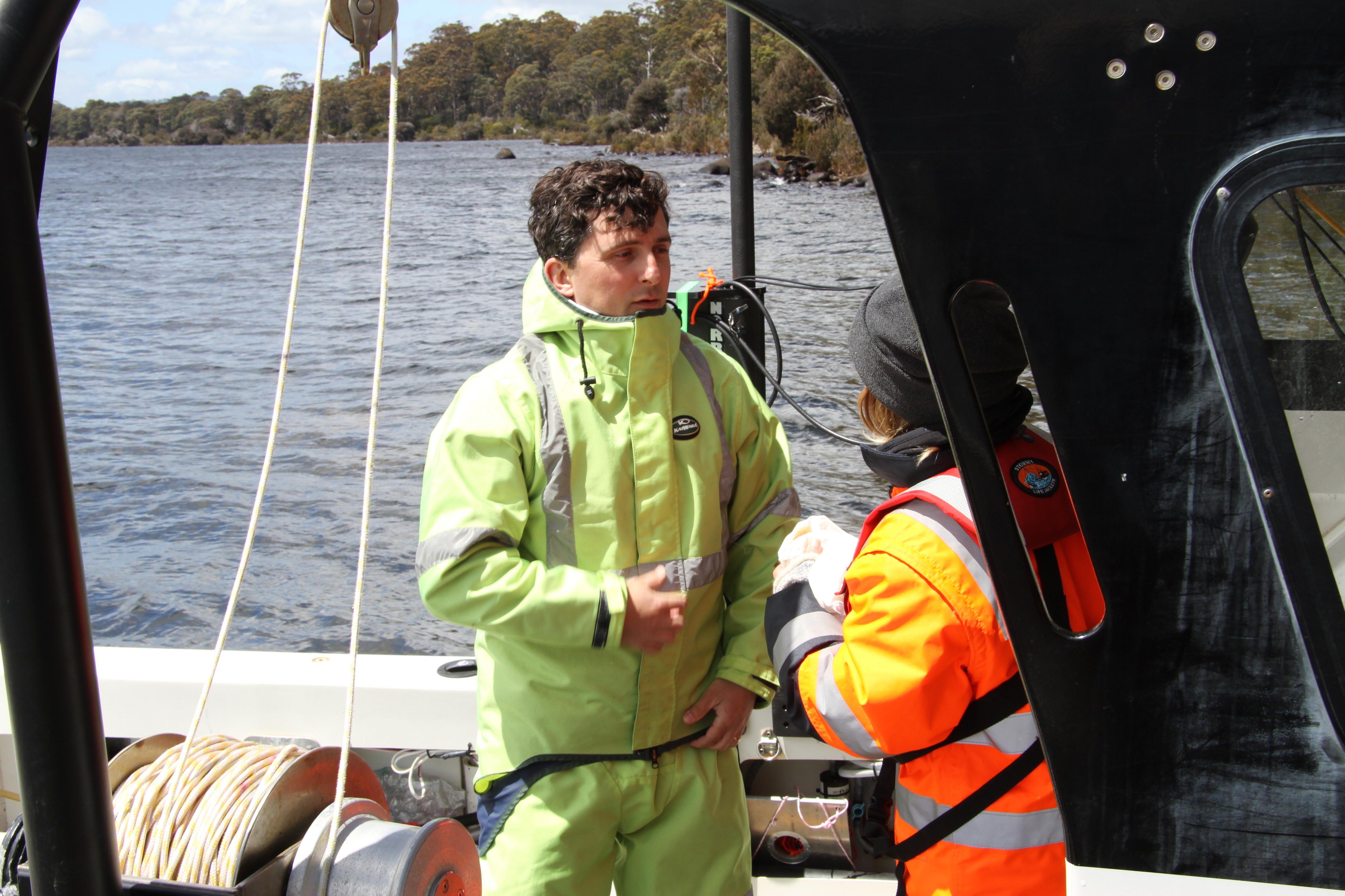a man in hi-vis yellow suit stands at the back of a boat