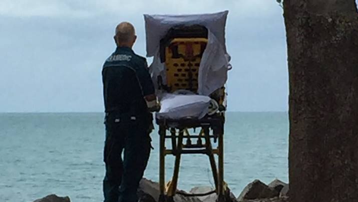 A Queensland Ambulance Service paramedic stands by a palliative patient in a stretcher by a beach in Hervey Bay