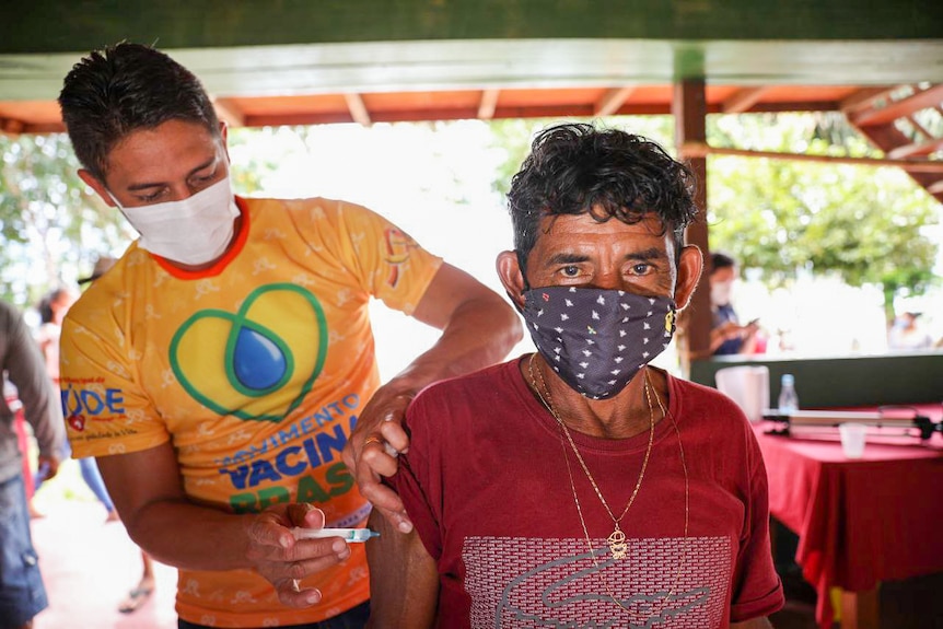 A man in a face mask gets an injection in his shoulder 