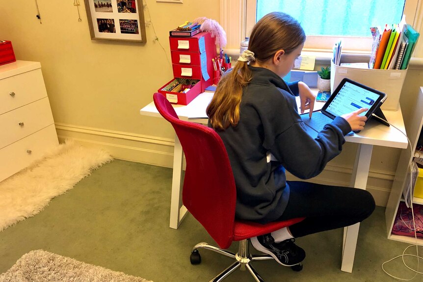 A girl looking at a tablet computer on a desk at her home.