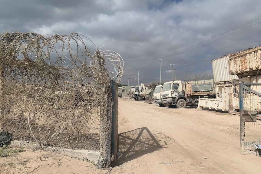 Barbed wire fence and a gate with trucks in a carpark.