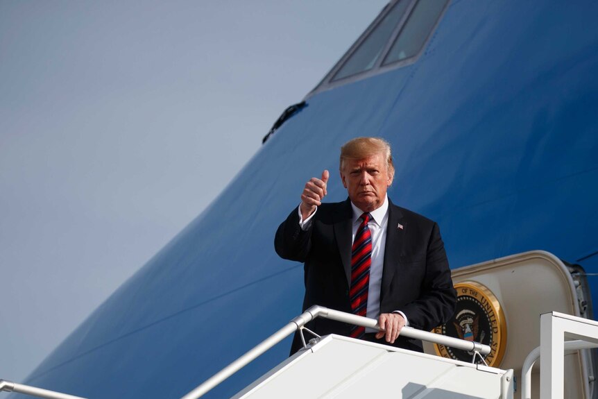 Donald trump stands at the door of his airplane showing a thumbs up