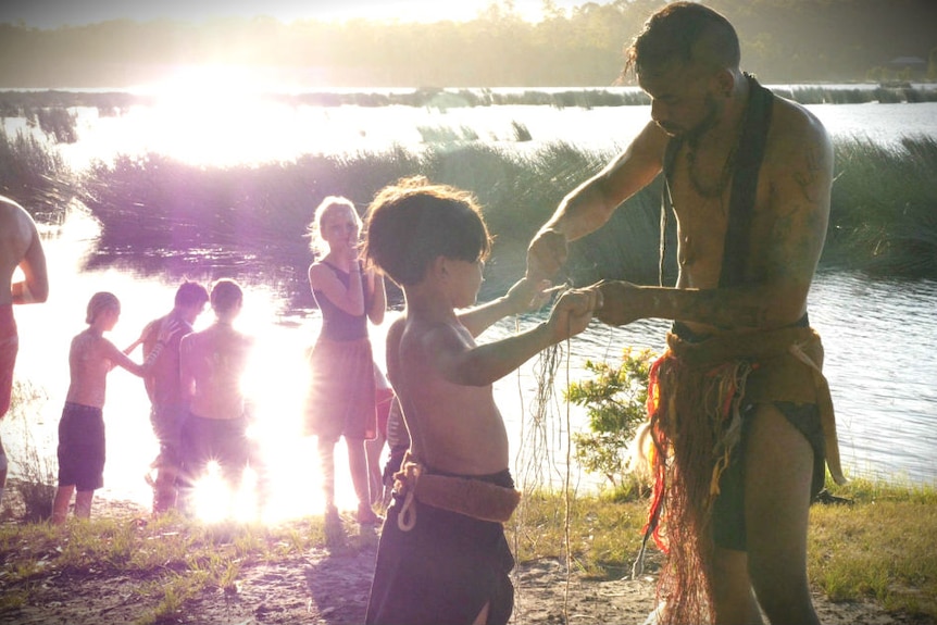 Aboriginal dancers standing near a lake get ready to perform