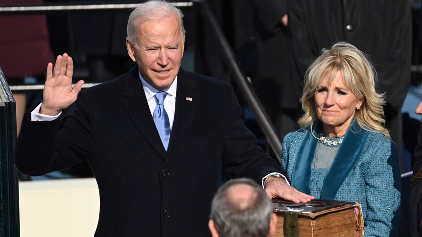 Joe Biden stands with one hand up and another on a bible.