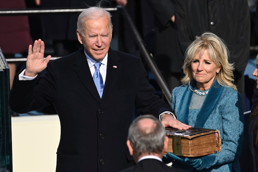 Joe Biden stands with one hand up and another on a bible.