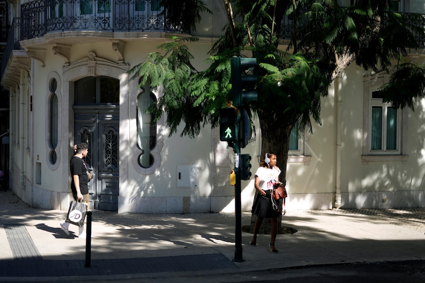 A woman crosses a street lined with jacaranda trees