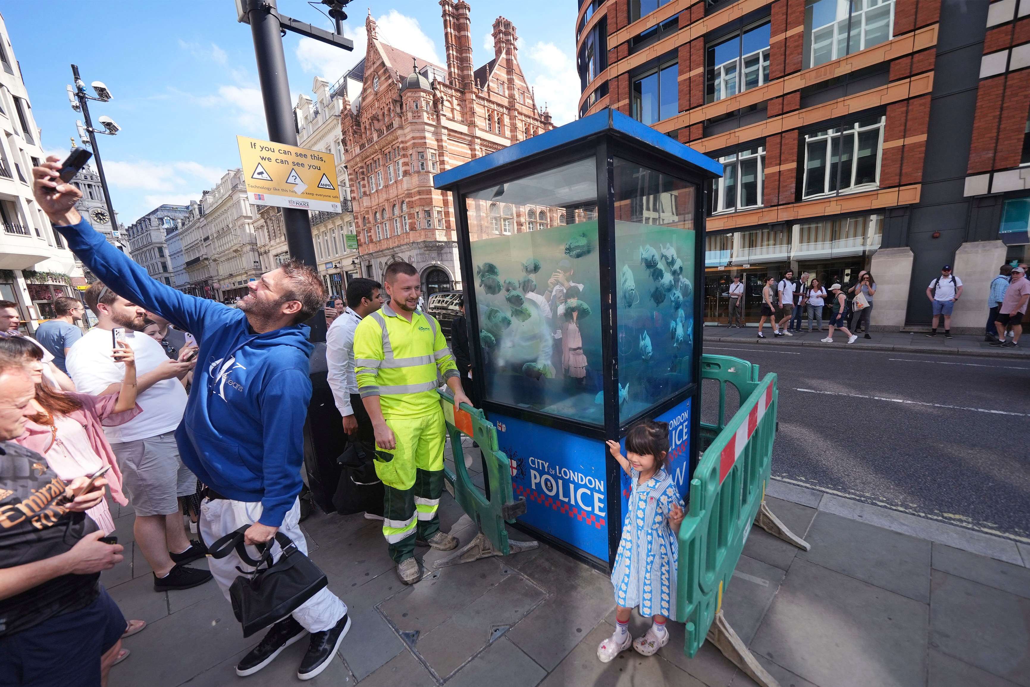 A crowd of people take photos in front of a police box painted with a school of piranhas 