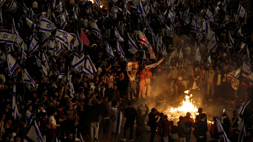 A large crowd of people gather around a fire in a protest at night in Israel.