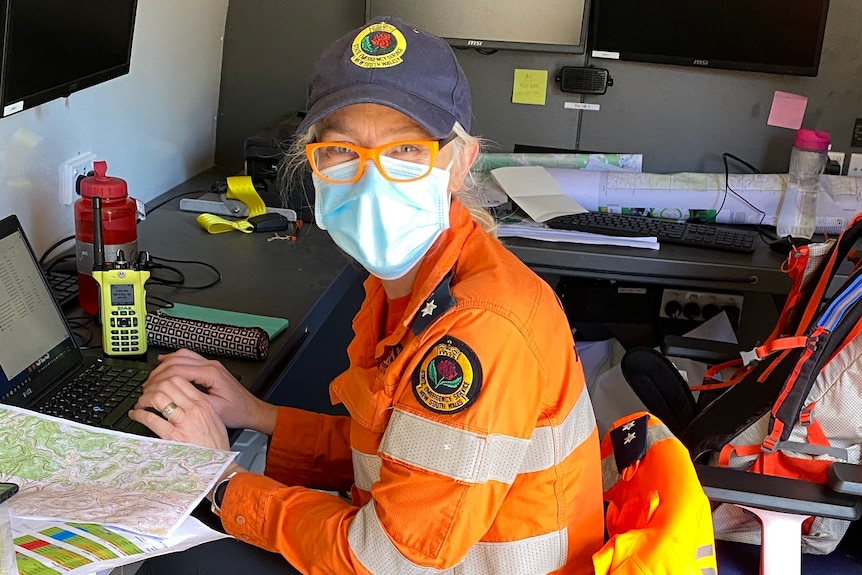 A woman in an orange uniform and COVID-19 mask sitting at a computer.