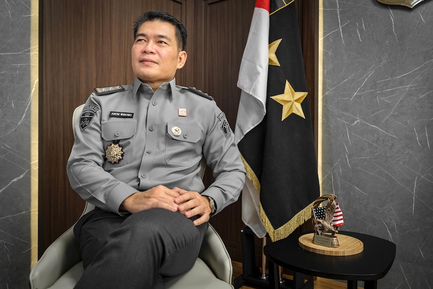 A policeman sitting on a chair in front of a flag