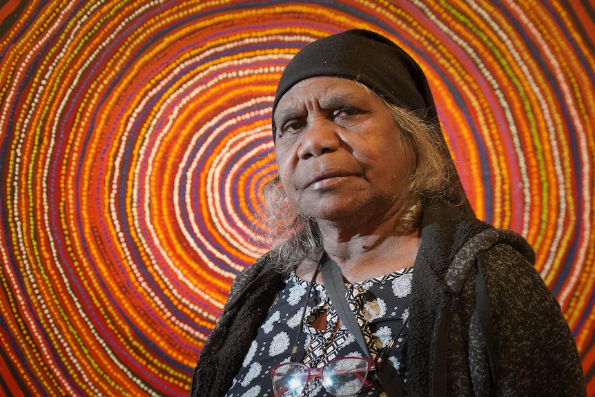 Alison Carroll stands in front of an Indigenous artwork.
