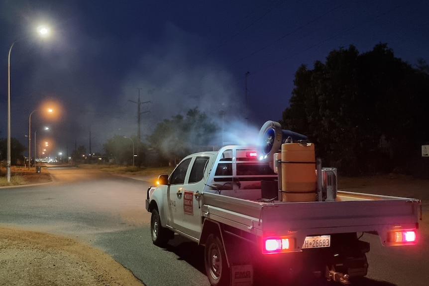 A machine sprays fog into the night sky from the back of a truck
