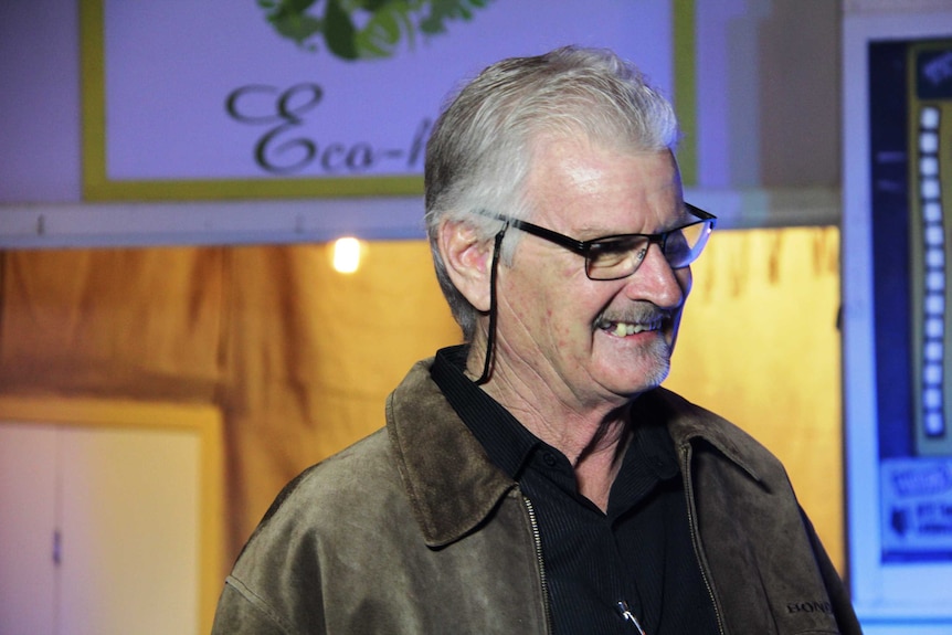 "Butch' Lenton smiling away from the camera, wearing his glasses. Blurred background.