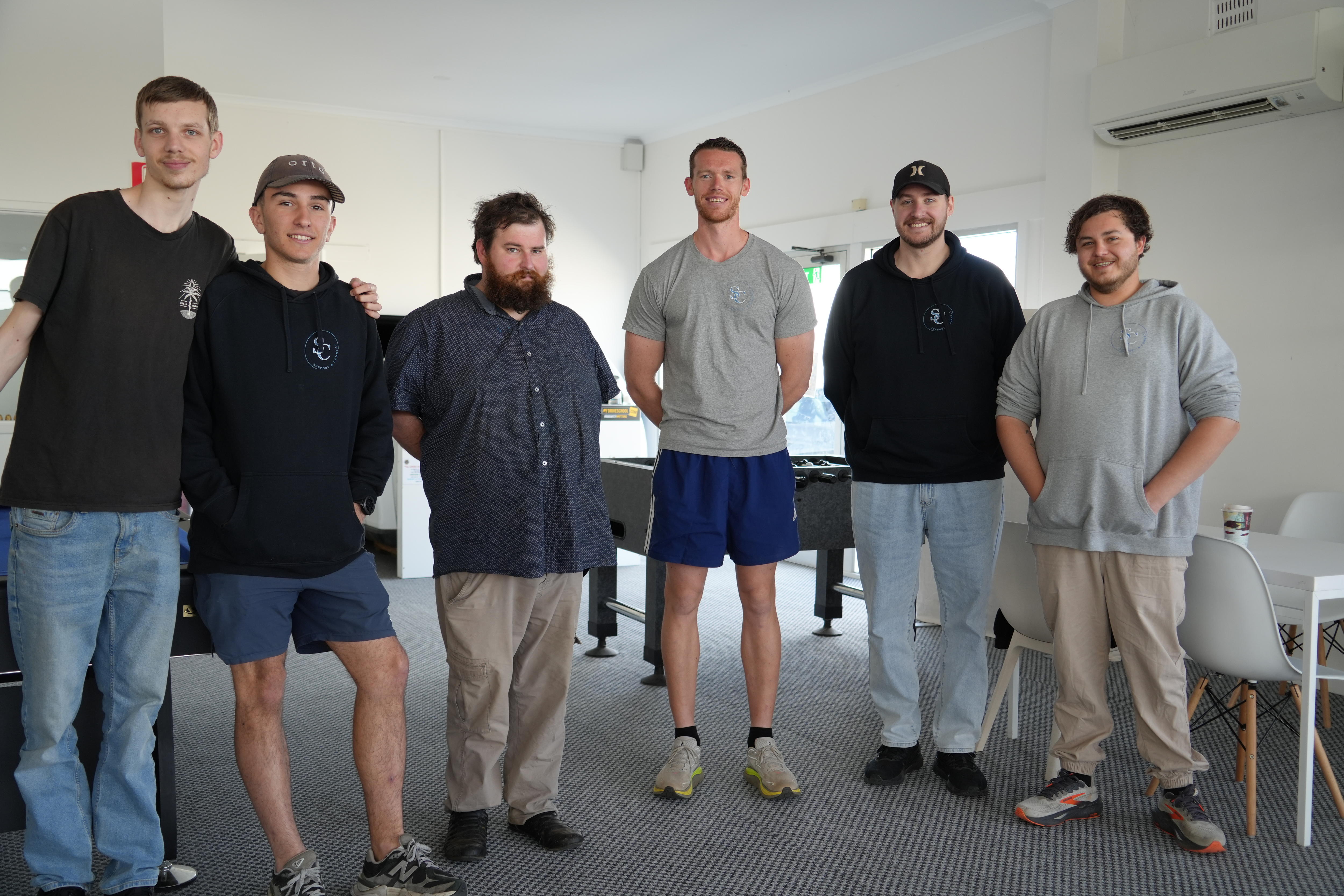 A line of men in various attire standing in a room smiling.