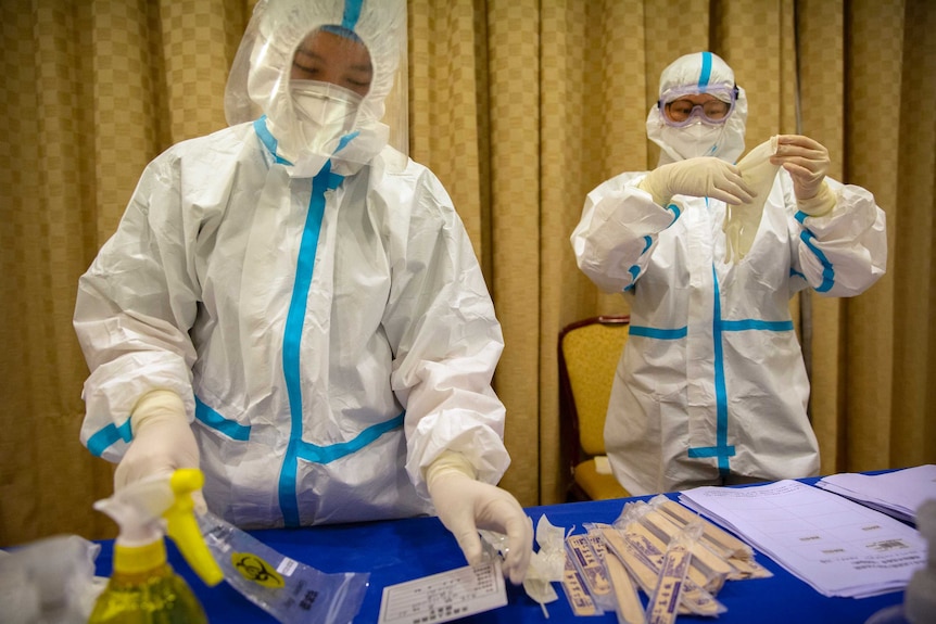 Workers in protective suits prepare to administer a COVID-19 test