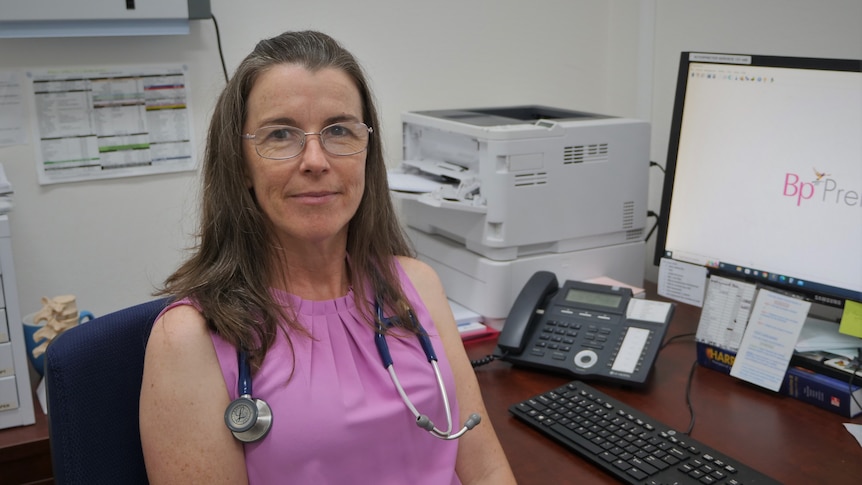 Woman in pink sleeveless shirt with stethoscope around her neck, sit in her doctor's office