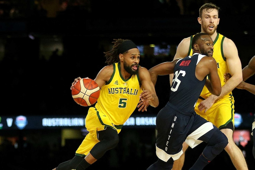 A male basketballer runs and dribbles the ball while marked by an opponent.